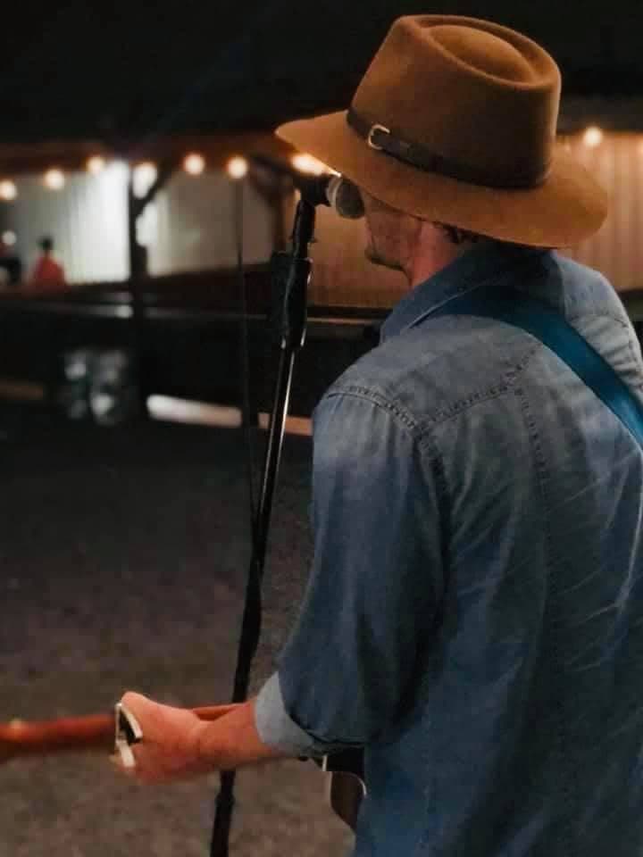 Nate Kelley in a cowboy hat singing at a microphone in a small venue